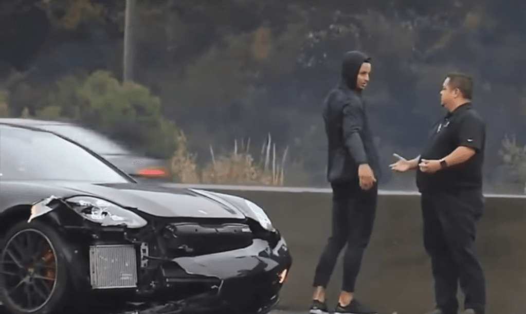 Curry conversando con otra persona al lado de su automóvil mientras en primer plano se observan los daños luego de la colisión.